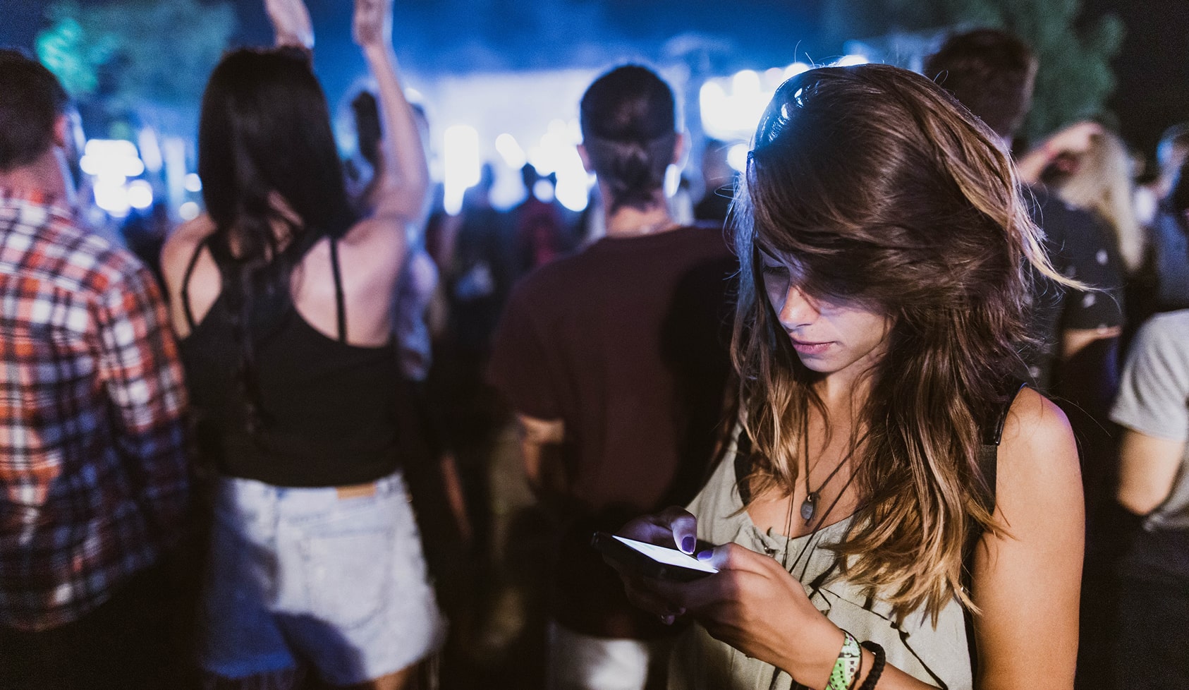 A brown haired woman looking down at her phone during a concert, donating.
