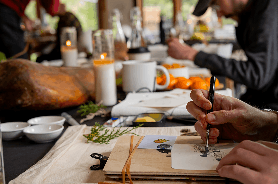 Close-up of hands sketching at a candlelit table